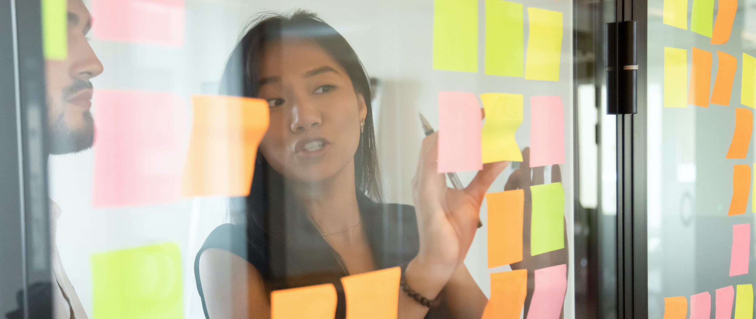  A woman standing in front of a glass board adorned with sticky notes.
