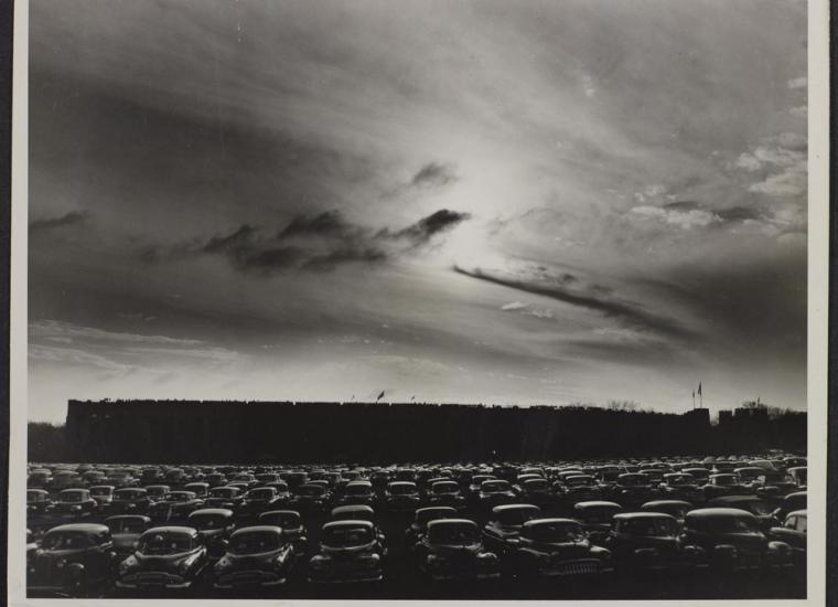 Black and white image of Palmer Memorial Stadium from a parking lot lined with cars